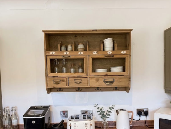A rustic wooden wall-mounted hutch cabinet with glass-front upper sections and drawers below, styled in a kitchen setting with a wooden countertop, toaster, coffee maker, kettle, and microwave.